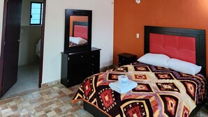 A bedroom with a wooden ceiling, a patterned bedspread, a red headboard, and a small bedside table.