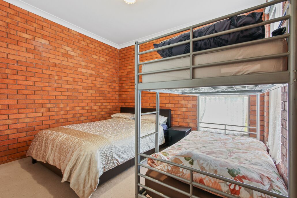 Una habitación con pared de ladrillo, dos literas, una ventana y una cama con colcha estampada.