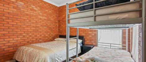 Una habitación con pared de ladrillo, dos literas, una ventana y una cama con colcha estampada.