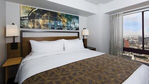 A hotel room with a large bed, a cityscape painting above the bed, a view of the city through a large window, and two bedside lamps. - Marriott Vacation Club, 1-Bedroom San Diego Suite (San Diego)