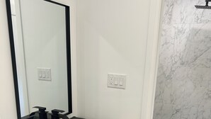 Uma casa de banho moderna com lavatório preto, gavetas de madeira, um espelho e um chuveiro com azulejos de mármore.