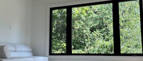 A room with a white sofa, large windows, and a wooden ceiling.