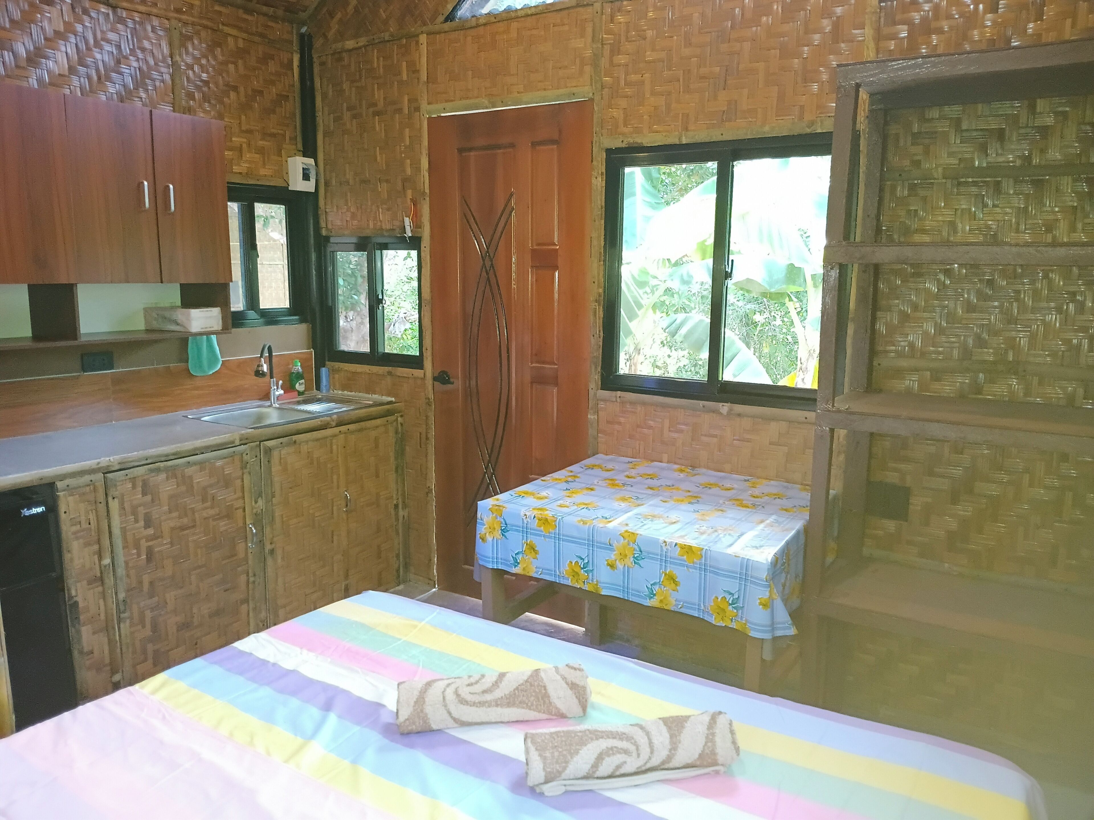 A room with a bed, a small table, a window, and a kitchen area.