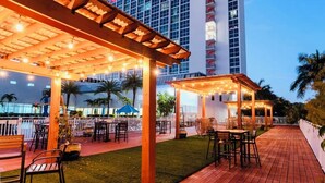 A hotel with outdoor seating, a covered patio, and a tall building in the background.