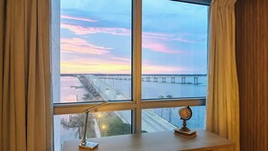 A room with a large window overlooking a bridge and water during sunset.
