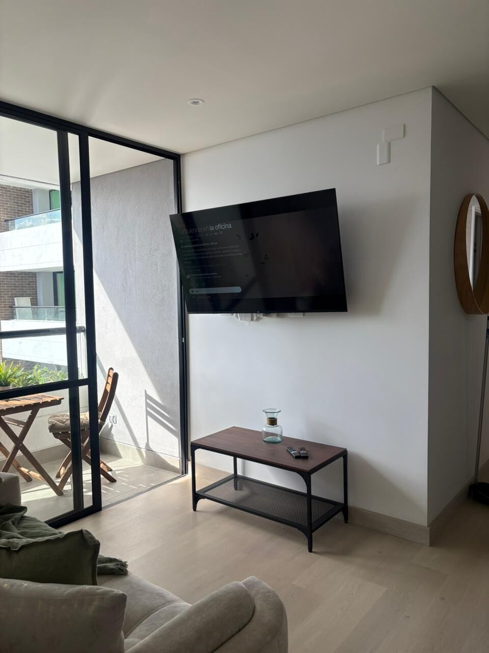 Ein modernes Wohnzimmer mit Flachbildfernseher an der Wand, einem kleinen Couchtisch und einer Couch.