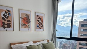 A bedroom with a bed, pillows, a bedside table, and a window with a cityscape view. - Modern Apartment in El Poblado | Excellent Location (Medellín)
