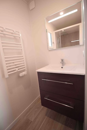 Een badkamer met een wit wastafel, een donker kastje en een spiegel erboven.