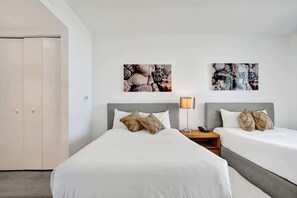 Quarto de hotel com duas camas, uma mesa de cabeceira com abajur e uma obra de arte na parede.