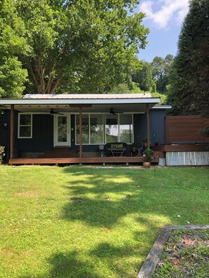 Ein eingeschossiges Haus mit einer Veranda, einer kleinen Terrasse und einem Rasen.