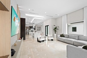 A modern living room with a sofa, chairs, a TV, and a kitchen in the background. - El Castillito (Miami)