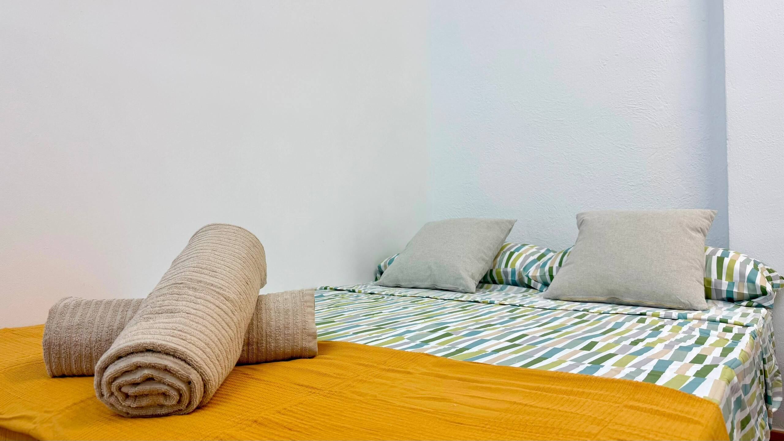 A bed with a yellow blanket, rolled towels, and two pillows.