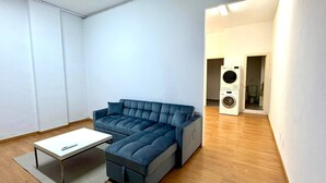 Una sala moderna con un sofá, una mesita y una lavadora al fondo.