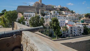Una fortaleza histórica con un cañón, con vistas a un pueblo densamente poblado de arquitectura tradicional.