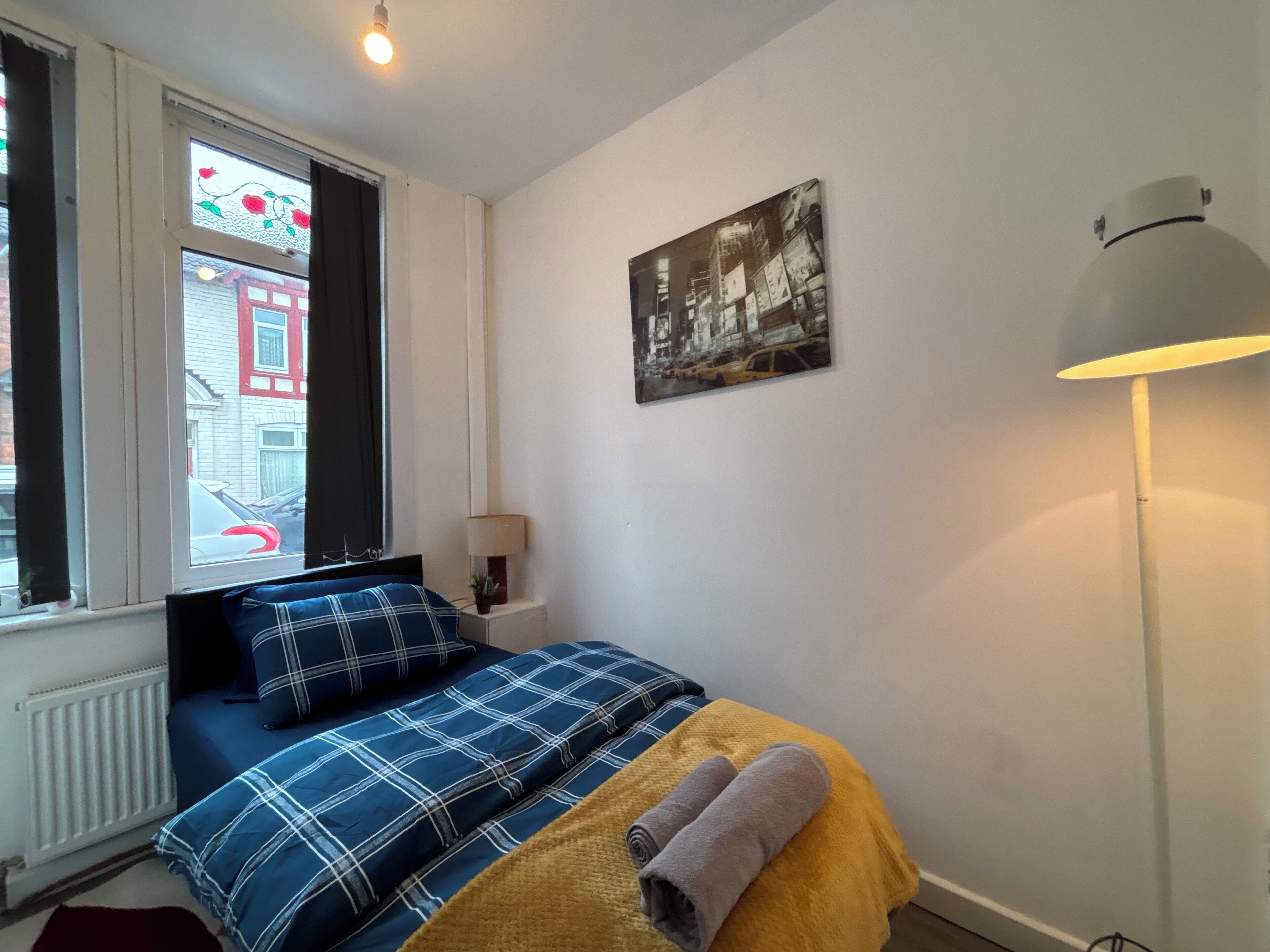 Ein Schlafzimmer mit einem Bett, einem Fenster, einer Lampe und einem Wandbild.