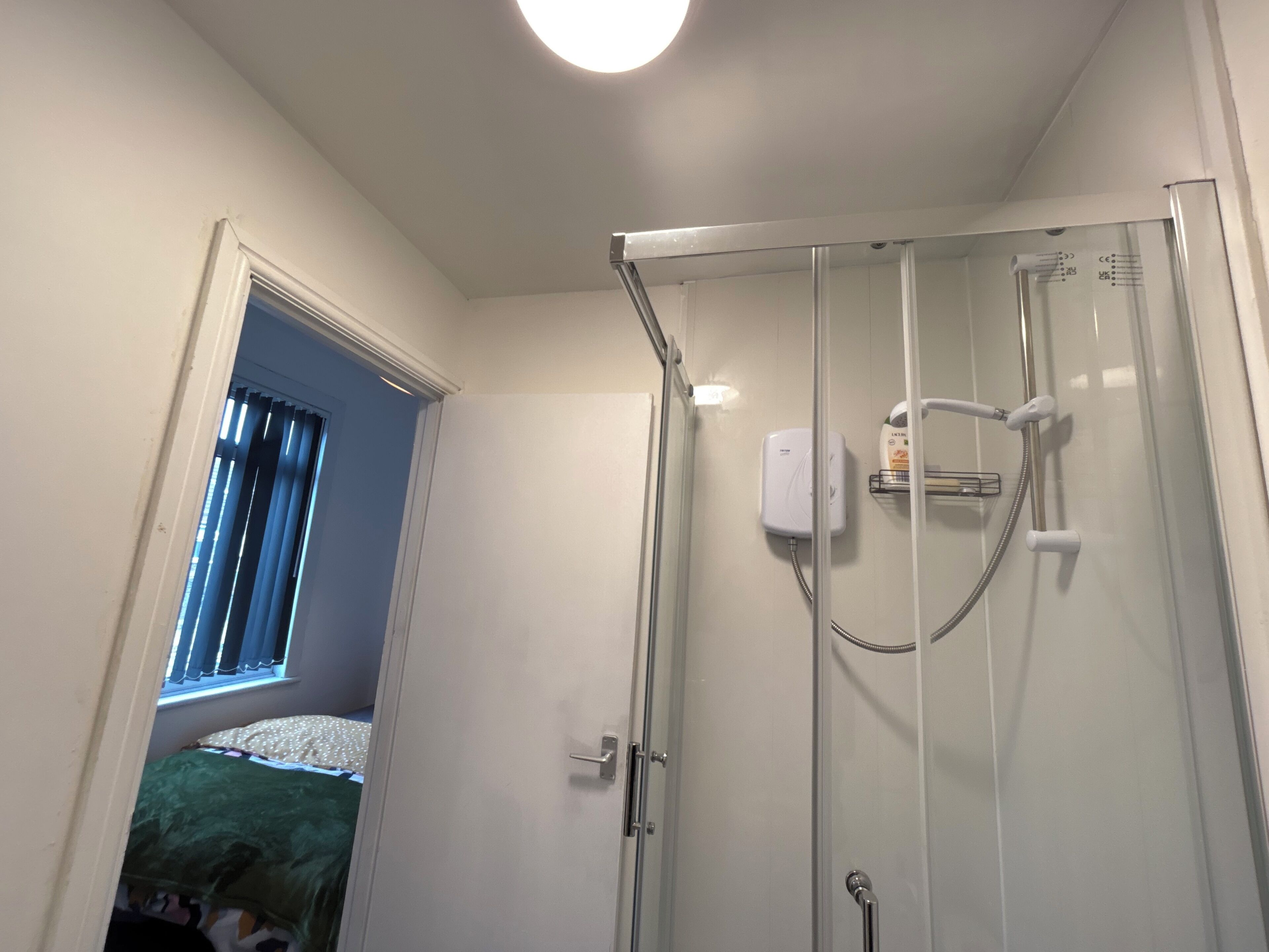 A glass-enclosed shower with a handheld showerhead and a wall-mounted control panel.