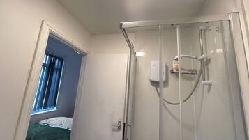 A glass-enclosed shower with a handheld showerhead and a wall-mounted control panel.