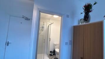 Een badkamer met een douche, toilet en een houten garderobe.