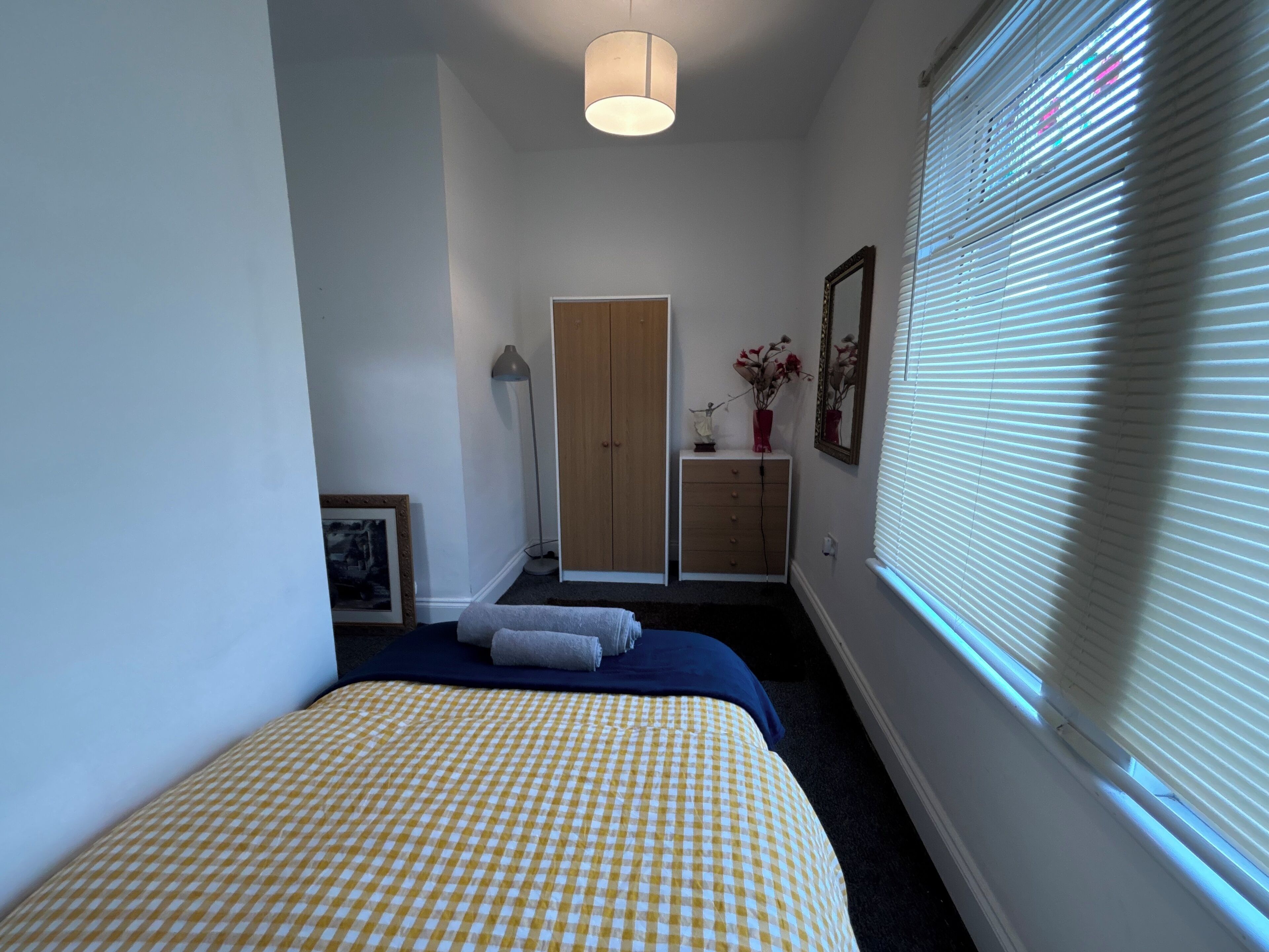 A bedroom with a bed, a wardrobe, a desk, a lamp, and a window with blinds.