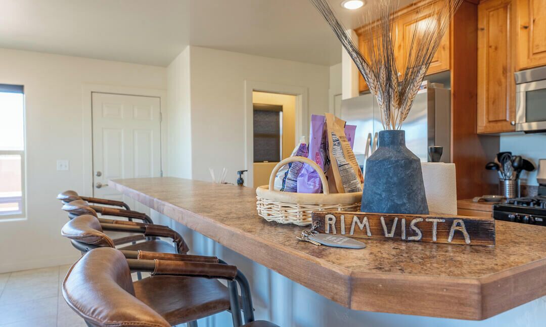 A kitchen with a wooden countertop, a vase with wheat stalks, and a basket of magazines.