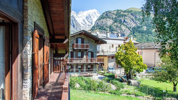 Ein Holzhaus mit Balkon, einer Steinmauer und einem Berg im Hintergrund.
