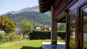 Bergblick von einem Holzhaus mit einem Steinpfeiler, einer Holzdielen-Terrasse und einem kleinen Stuhl.