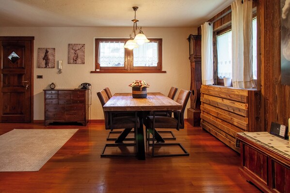Un coin repas avec une table en bois, des chaises, un lustre et une fenêtre avec des rideaux.