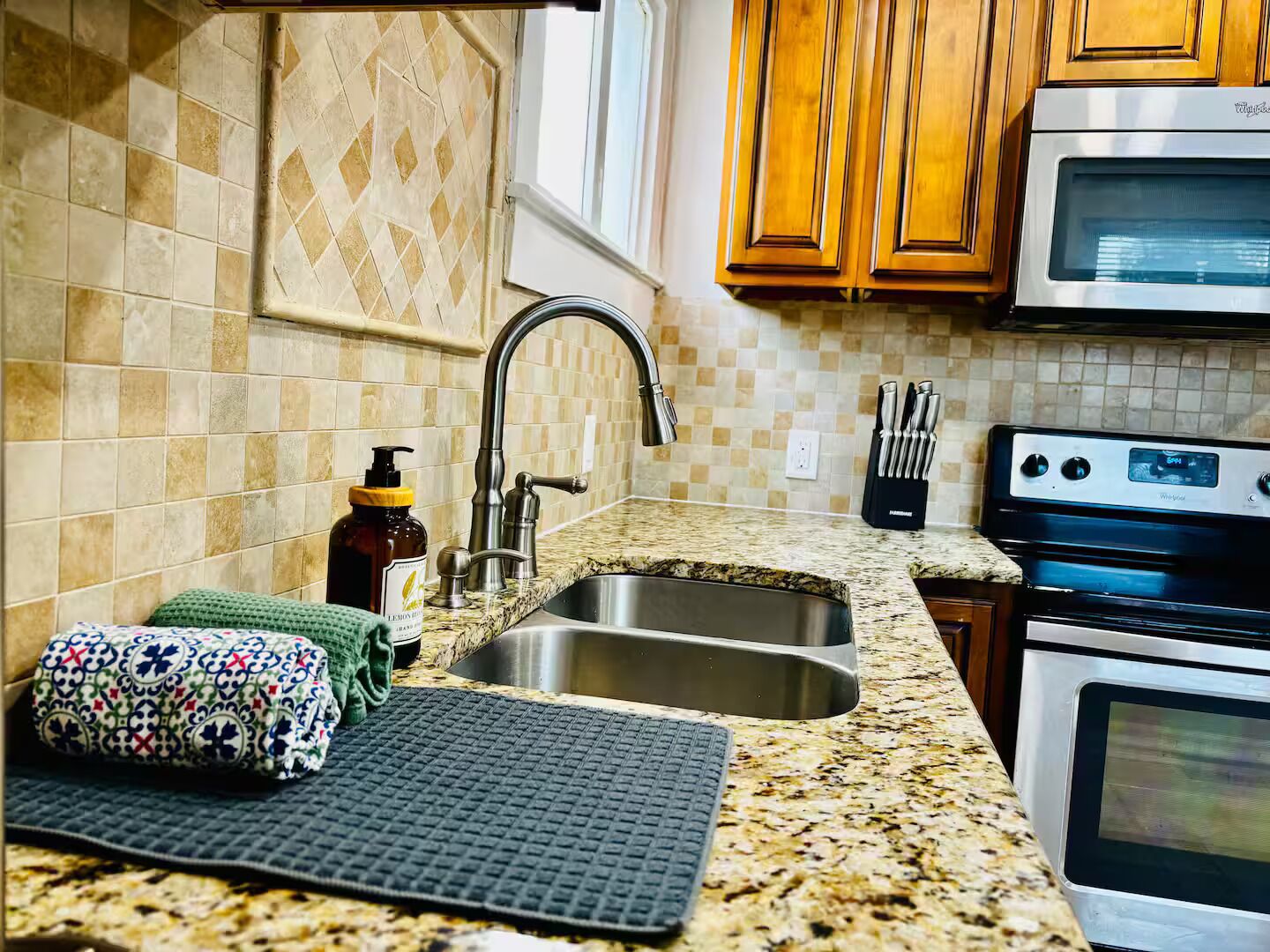 A kitchen with a granite countertop, stainless steel sink, wooden cabinets, a microwave, and an oven.