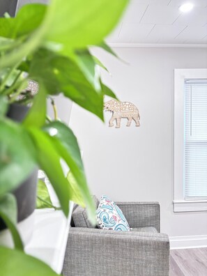 A room with a grey sofa, a patterned pillow, a wall-mounted elephant decoration, and a window with blinds. - HP Furniture Market <1 mi  & HPU <2 mi - Downtown -Brick Cottage (High Point)