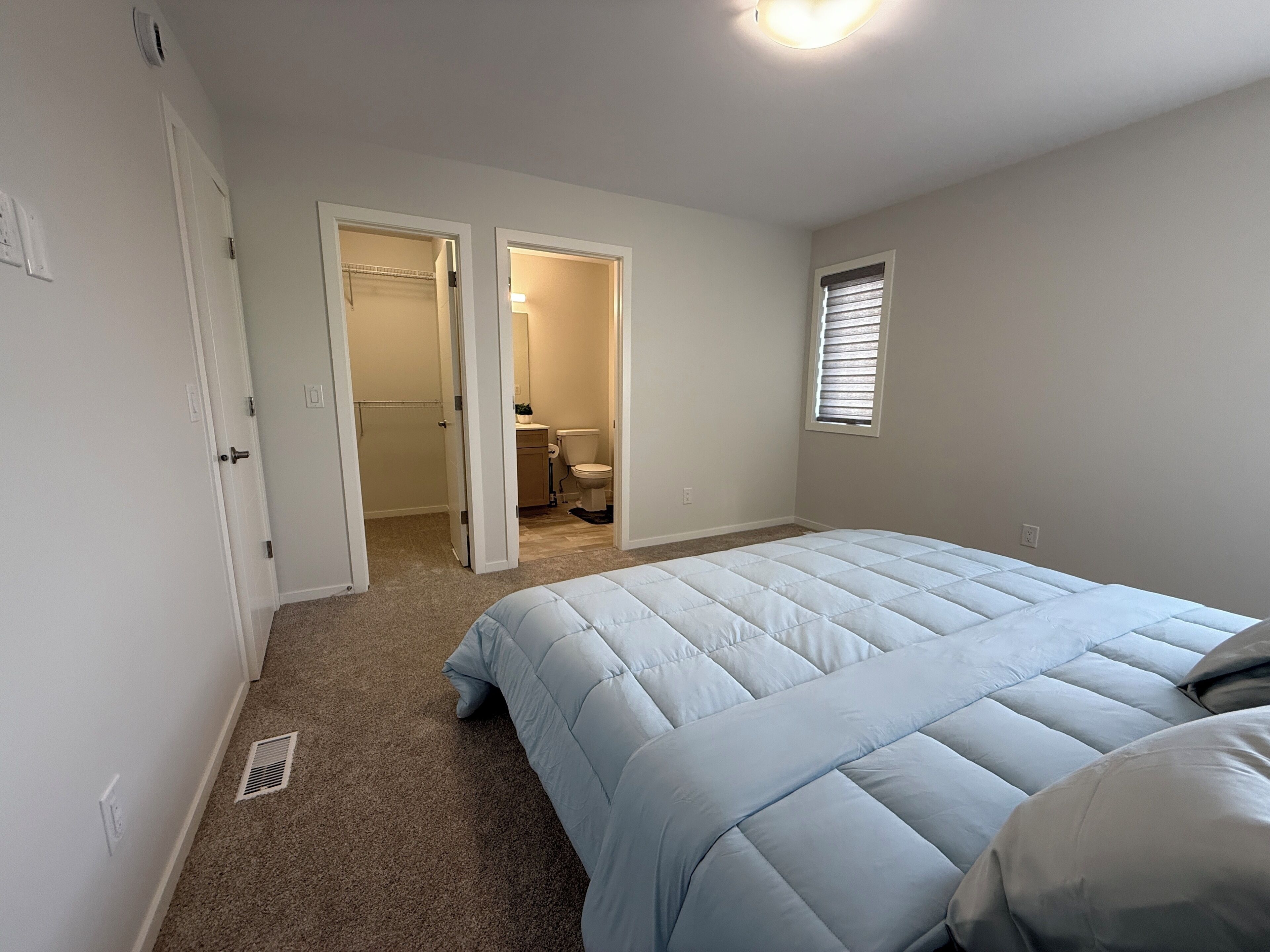 Un dormitorio con cama, ventana y puerta abierta que da a un baño.