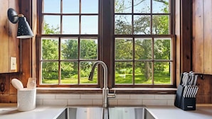 Uma cozinha com pia de aço inoxidável, janela com vista para o verde e porta-facas no balcão.