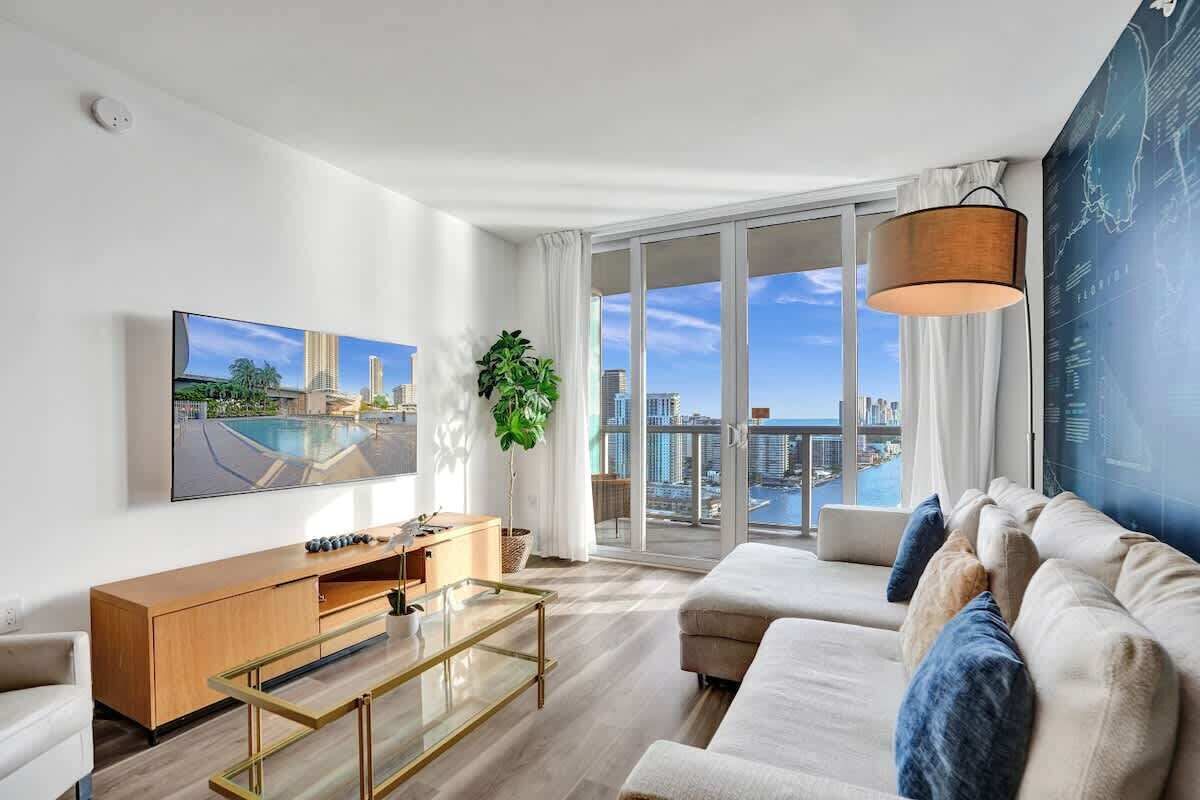 A modern living room with a large window, a flat-screen TV, a sofa, a coffee table, and a plant.