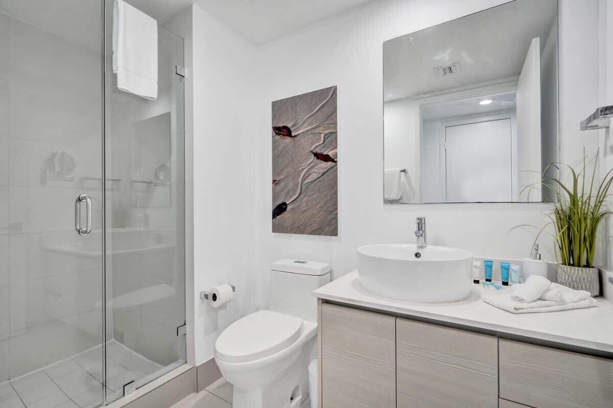 A modern bathroom with a glass shower enclosure, a white toilet, a large mirror, and a white sink with a countertop.
