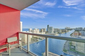 Ein Balkon mit roter Wand, einer Bank und Blick auf Stadt und Wasser.