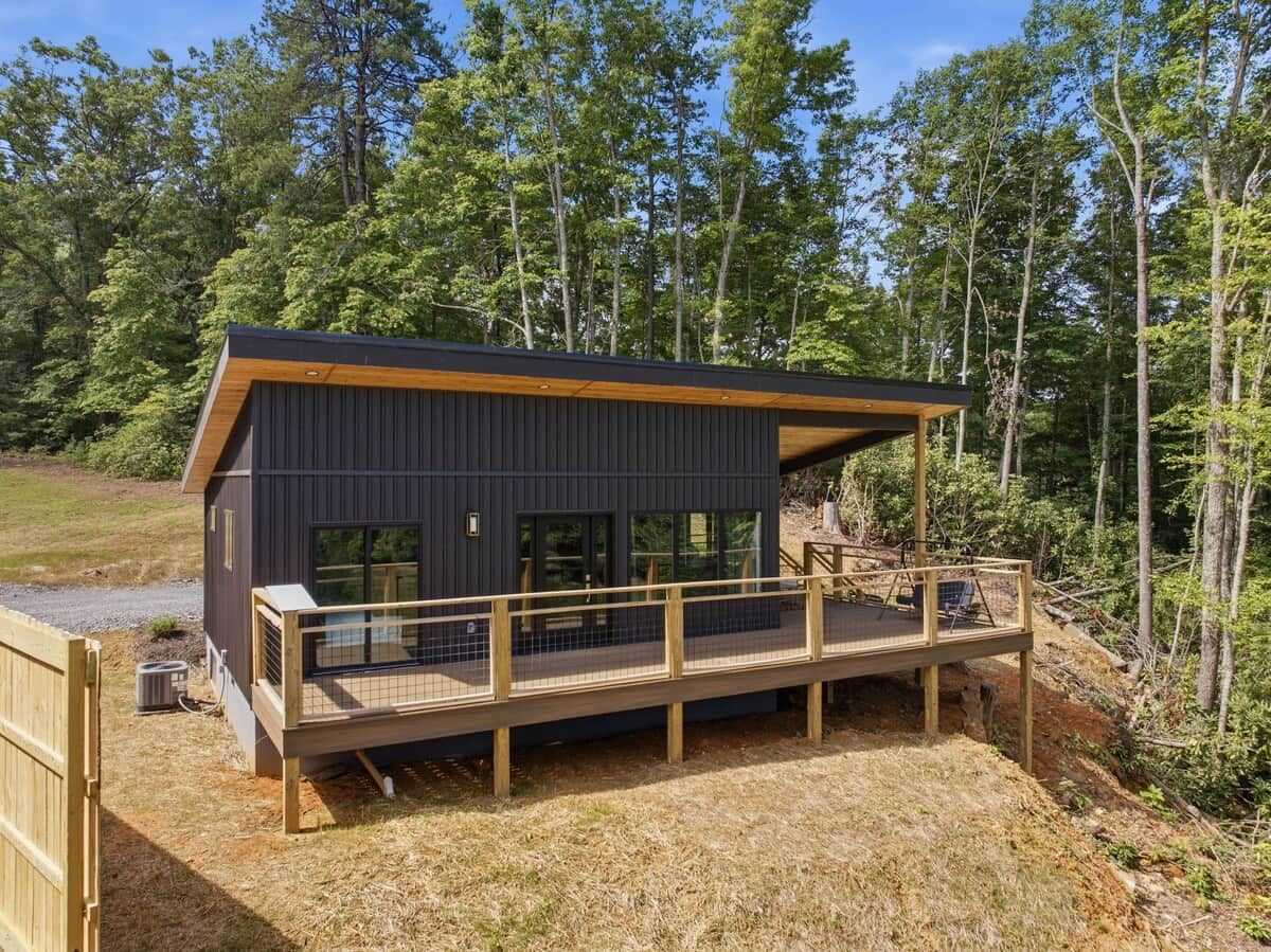 Une cabane moderne dotée d’une terrasse, entourée d’une forêt.