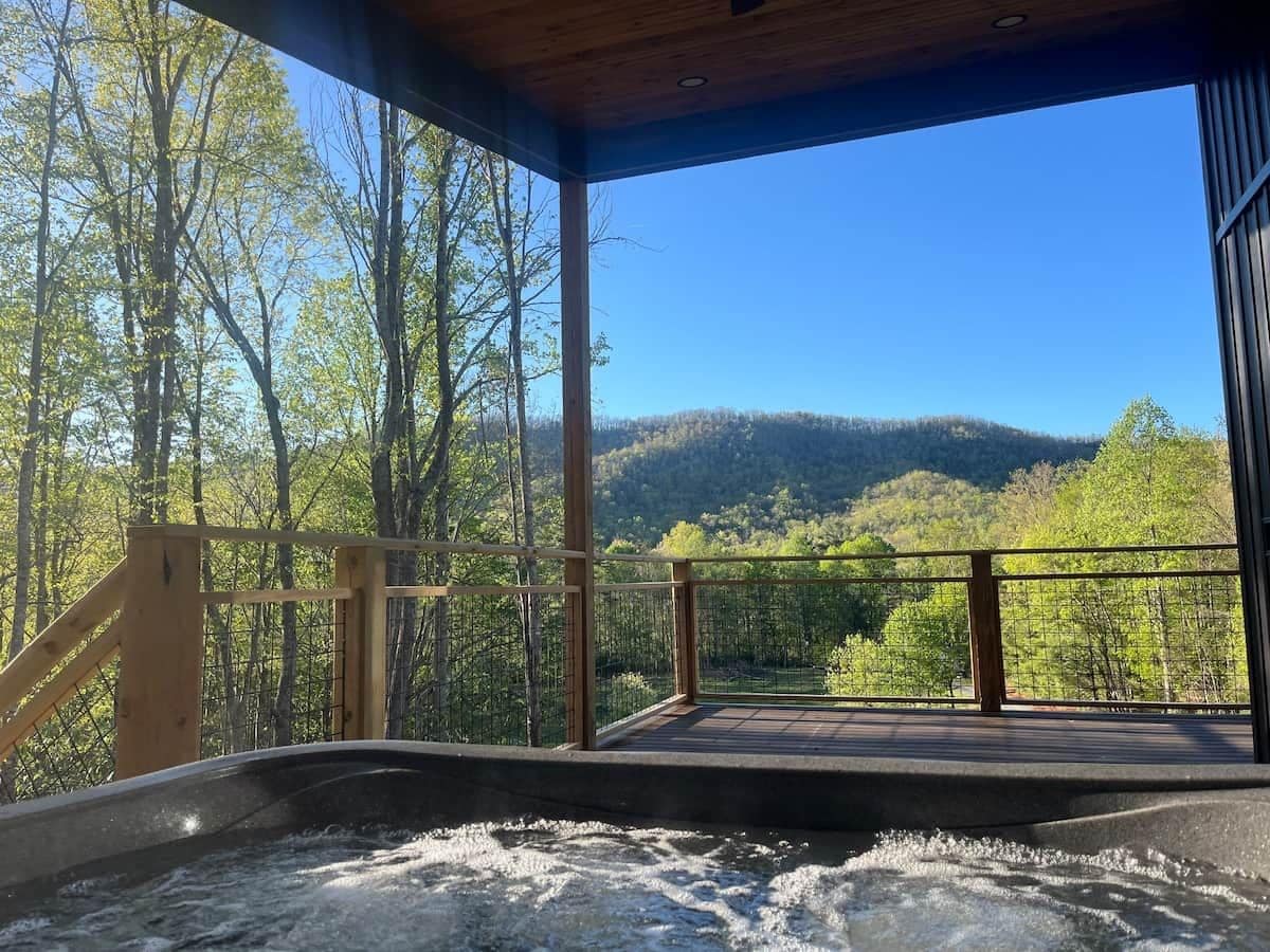 A hot tub area with a wooden deck and a view of a forested hillside.
