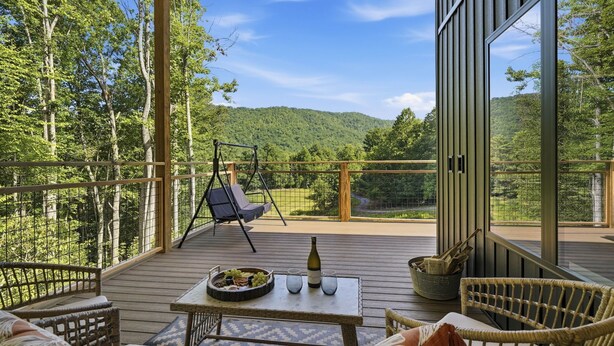 A wooden deck with wicker furniture, a swing chair, and a table with a bottle and glasses. - Cozy 1 bedroom cabin with a hot tub in the mountains of Elizabethton (Elizabethton)