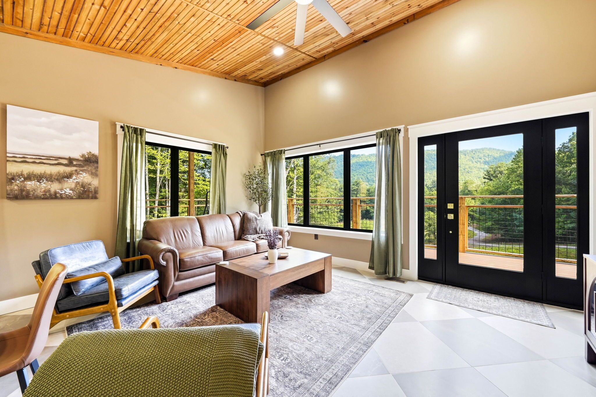 A spacious living room with a sofa, chairs, a coffee table, and large windows offering a view of greenery.