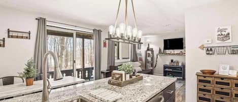 A modern kitchen with a granite countertop, stainless steel sink, and a pendant light fixture.
