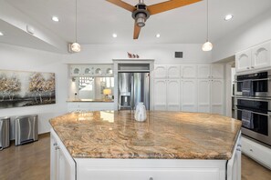 A kitchen with a large granite island, white cabinetry, stainless steel appliances, and a ceiling fan. - Sundance  Resort Style Home in the Foothills (Tucson)