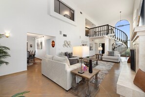 A spacious living area with a high ceiling, a staircase, and a dining area.