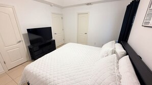 Un dormitorio con cama, televisor, cómoda y dos puertas.