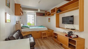 A compact room with a bed, a sofa, a TV, wooden shelves, and a desk. - Charming studio just a stone's throw from Les Halles and the beaches (BIARRITZ)
