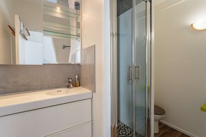 A modern bathroom with a glass shower enclosure, a white sink, and a toilet. - Charming studio just a stone's throw from Les Halles and the beaches (BIARRITZ)