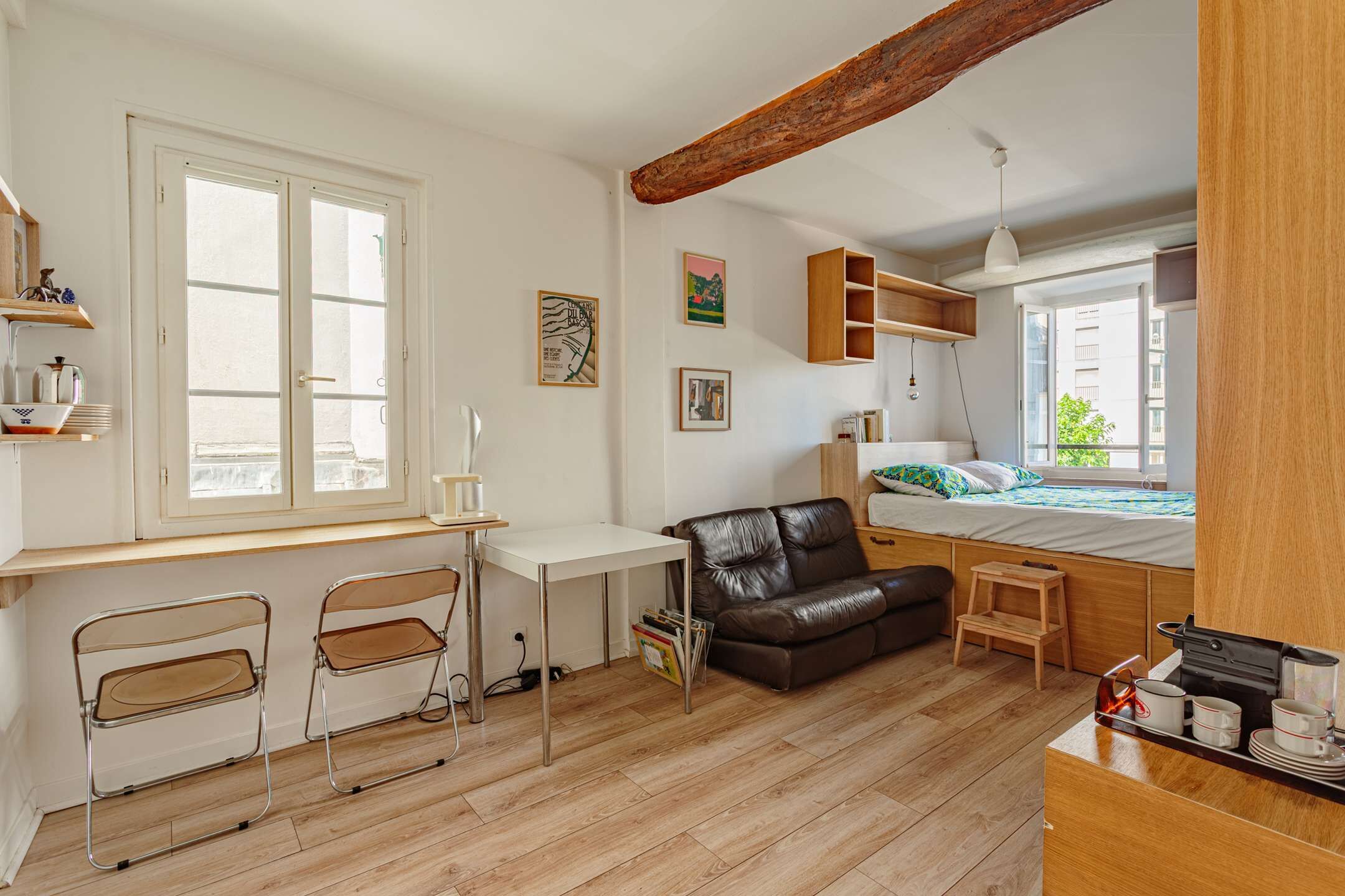 Une pièce de taille modeste, comprenant un bureau, deux chaises, un canapé, un lit et un petit tabouret.