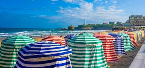 A beach with striped umbrellas and a lighthouse in the background. - Charming studio just a stone's throw from Les Halles and the beaches (BIARRITZ)