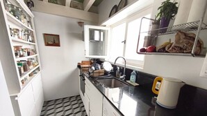 Ett kompakt kök med vita skåp, en svart bänkskiva, en diskho och ett fönster.