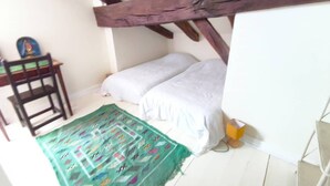 Ett litet, ombonat rum med ett sluttande tak, en säng med vita sängkläder, en färgglad matta, en trästol och ett litet bord.