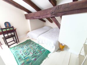 A small, cozy room with a sloped ceiling, a bed with white bedding, a colorful rug, a wooden chair, and a small table. - SAINT-JEAN DE LUZ, CENTRE HISTORIQUE, QUAI DE L'INFANTE (ST JEAN DE LUZ)
