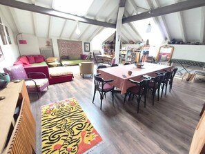Un loft espaiós amb un sostre alt, una zona de menjador amb taula i cadires, un sofà, una catifes amb dibuixos i una prestatgeria.